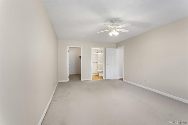 unfurnished bedroom with baseboards, a walk in closet, connected bathroom, and light colored carpet