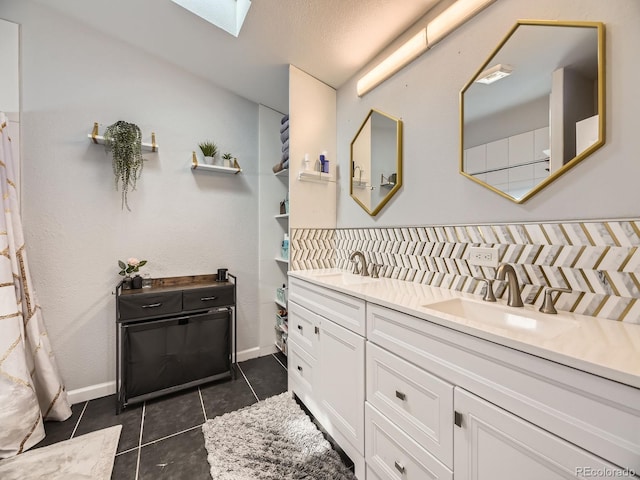 bathroom with a skylight, double vanity, tile patterned flooring, and a sink