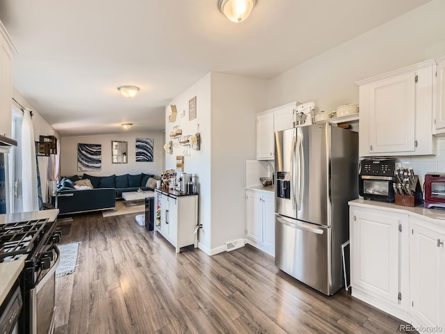 kitchen with dark wood-style floors, backsplash, appliances with stainless steel finishes, open floor plan, and white cabinetry