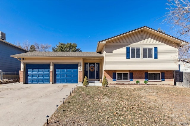 tri-level home with a garage, driveway, brick siding, and fence