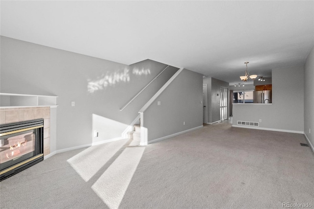 unfurnished living room with light colored carpet, a fireplace, and an inviting chandelier