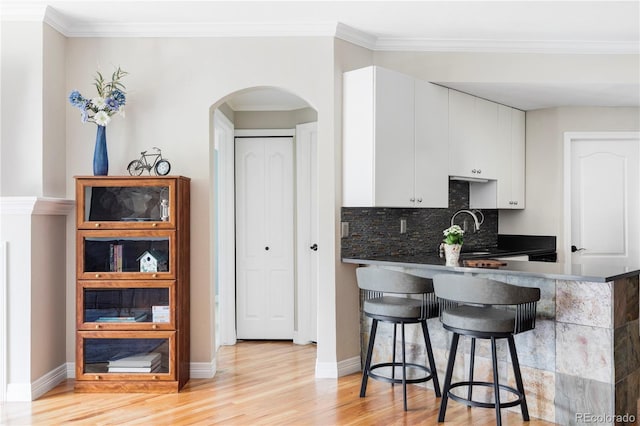 111 S Monroe St Unit B106, Denver, CO 80209 - kitchen featuring arched walkways, light wood-type flooring, a kitchen breakfast bar, white cabinets, and dark countertops