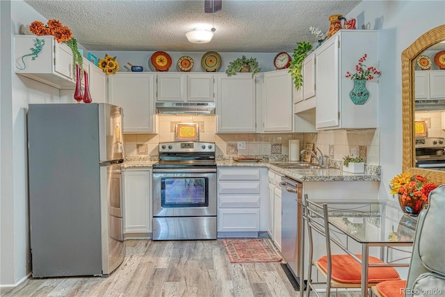 kitchen featuring decorative backsplash, light hardwood / wood-style flooring, light stone counters, stainless steel appliances, and white cabinets