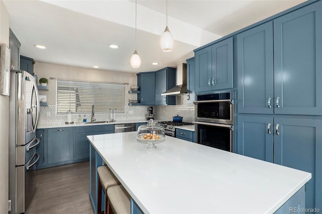 kitchen with sink, decorative light fixtures, wall chimney range hood, appliances with stainless steel finishes, and dark hardwood / wood-style floors