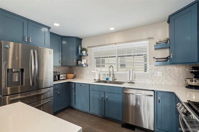 kitchen with appliances with stainless steel finishes, backsplash, dark hardwood / wood-style flooring, blue cabinetry, and sink