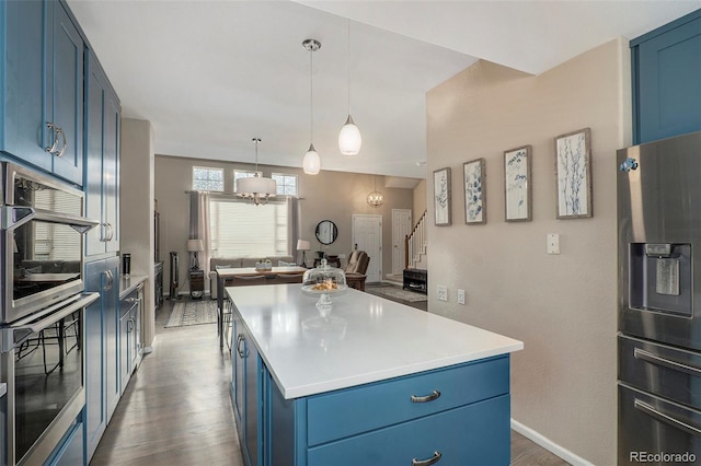 kitchen with blue cabinets, dark wood-type flooring, appliances with stainless steel finishes, and a kitchen island