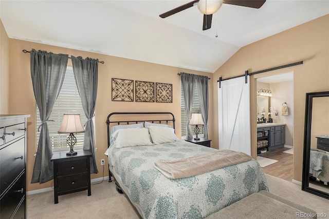 bedroom featuring vaulted ceiling, a barn door, ceiling fan, ensuite bath, and light carpet