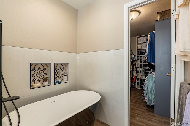 bathroom with a tub to relax in, a textured ceiling, and hardwood / wood-style flooring