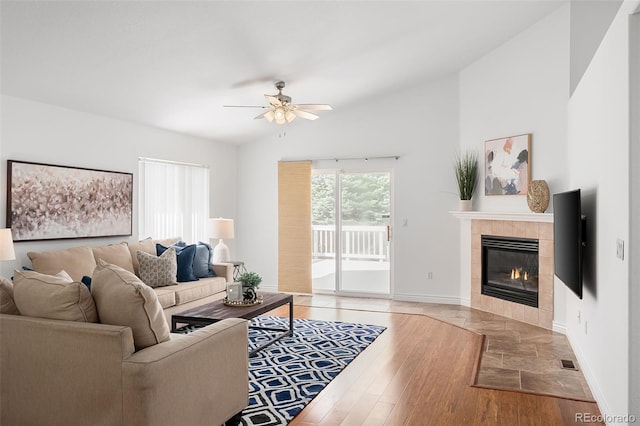 living room featuring visible vents, baseboards, ceiling fan, light wood-type flooring, and a tile fireplace