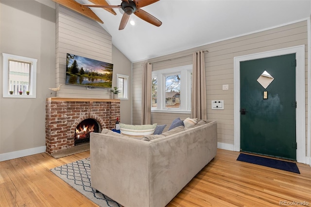 living room featuring vaulted ceiling, wood finished floors, a ceiling fan, baseboards, and a brick fireplace
