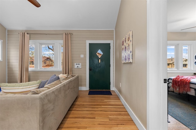 foyer with light wood-style floors, a ceiling fan, baseboards, and wooden walls