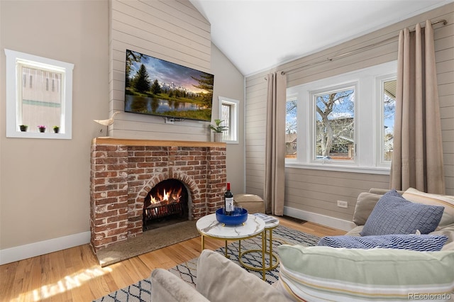 living area with wood finished floors, vaulted ceiling, baseboards, and a brick fireplace