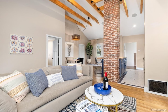 living area featuring light wood finished floors, visible vents, beamed ceiling, baseboards, and high vaulted ceiling