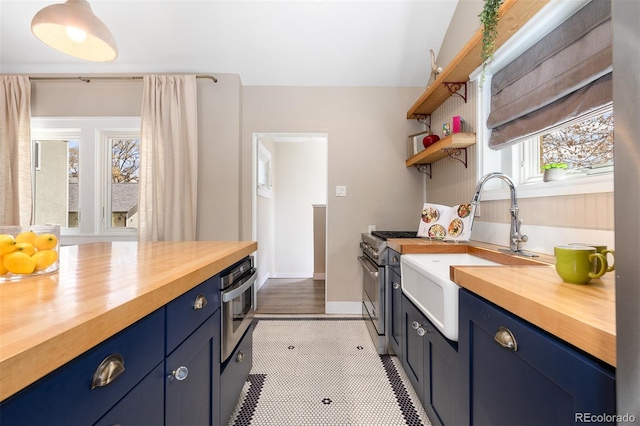 kitchen featuring stainless steel oven, wood counters, blue cabinetry, and a sink