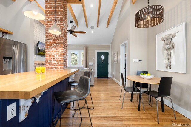 kitchen featuring baseboards, light wood-style floors, butcher block countertops, beamed ceiling, and high vaulted ceiling