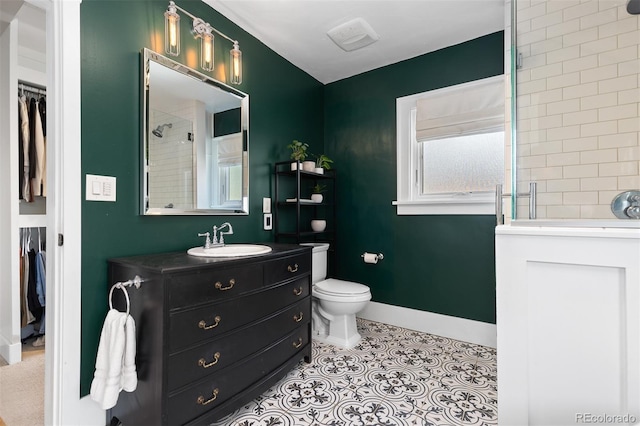 bathroom with toilet, a walk in closet, vanity, baseboards, and tiled shower
