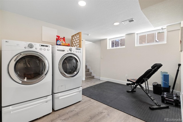 clothes washing area featuring washing machine and clothes dryer, light wood-type flooring, visible vents, baseboards, and laundry area