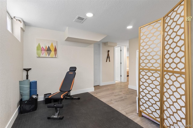 workout area with baseboards, a textured ceiling, visible vents, and light wood-style floors