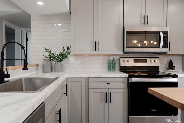 kitchen featuring light stone countertops, recessed lighting, a sink, stainless steel appliances, and backsplash