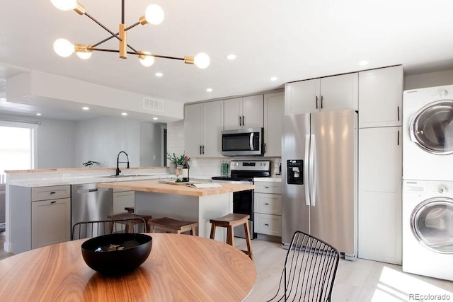 kitchen with tasteful backsplash, visible vents, stainless steel appliances, stacked washer / drying machine, and a sink