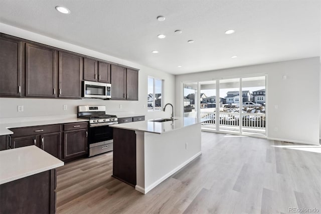 kitchen with appliances with stainless steel finishes, sink, a center island with sink, and light wood-type flooring