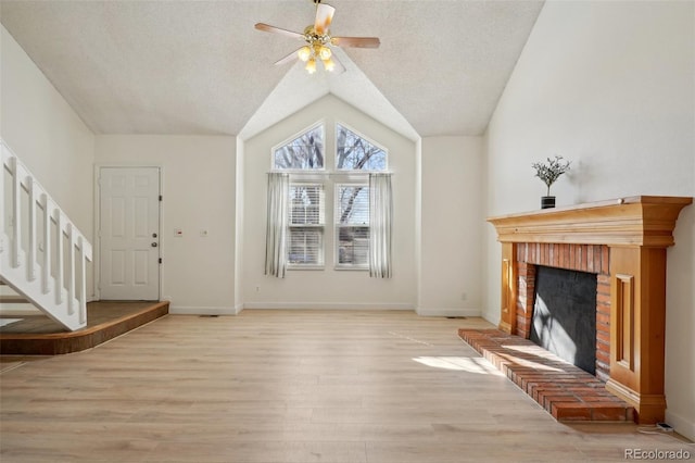 unfurnished living room featuring a fireplace, light wood finished floors, vaulted ceiling, a textured ceiling, and baseboards