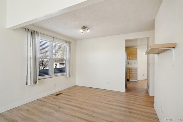 interior space featuring a textured ceiling, light wood finished floors, visible vents, and baseboards