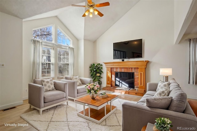 living area with high vaulted ceiling, a fireplace, a ceiling fan, visible vents, and light wood-style floors