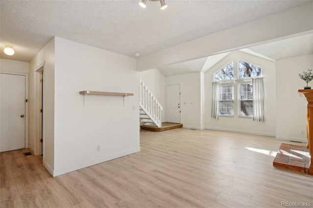 unfurnished living room with stairs, a textured ceiling, light wood-type flooring, and lofted ceiling