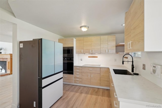 kitchen featuring stainless steel microwave, oven, freestanding refrigerator, light brown cabinets, and a sink