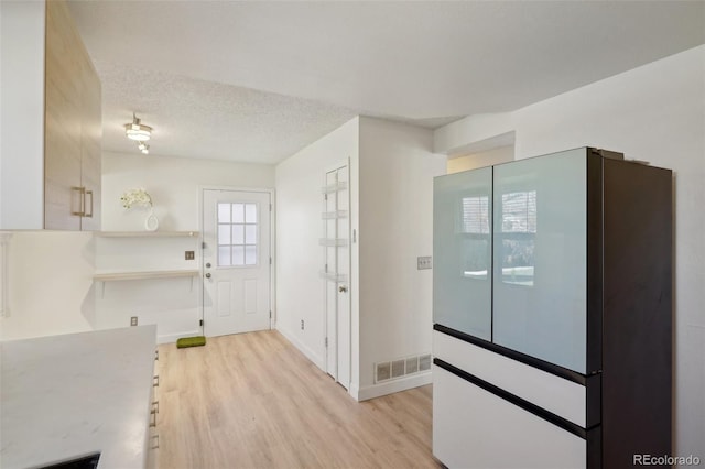 kitchen featuring baseboards, visible vents, a textured ceiling, and light wood finished floors