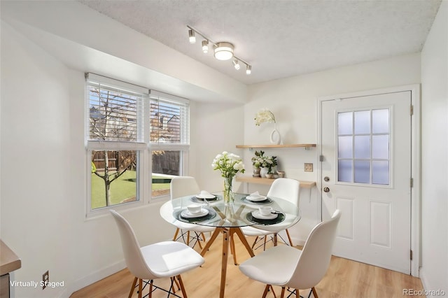 dining area featuring light wood finished floors, baseboards, and a textured ceiling