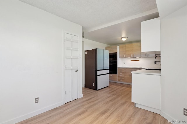 kitchen featuring a sink, light wood-style floors, black oven, freestanding refrigerator, and built in microwave