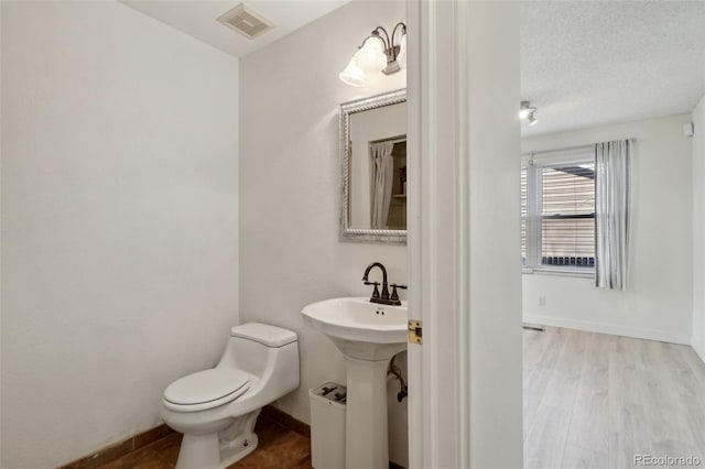 bathroom with baseboards, visible vents, toilet, wood finished floors, and a textured ceiling