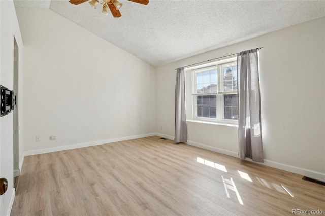 spare room featuring vaulted ceiling, a textured ceiling, baseboards, and wood finished floors