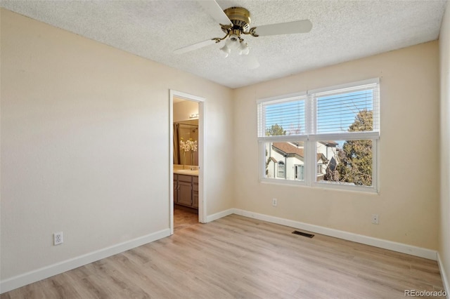 interior space featuring visible vents, baseboards, light wood-style flooring, ensuite bathroom, and a textured ceiling