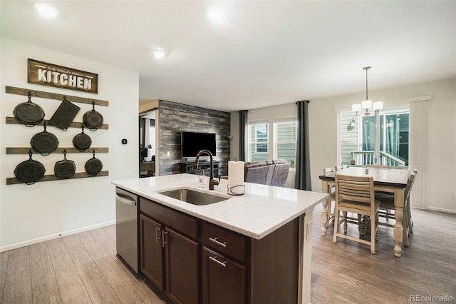 kitchen with sink, hanging light fixtures, a kitchen island with sink, light wood-type flooring, and stainless steel dishwasher