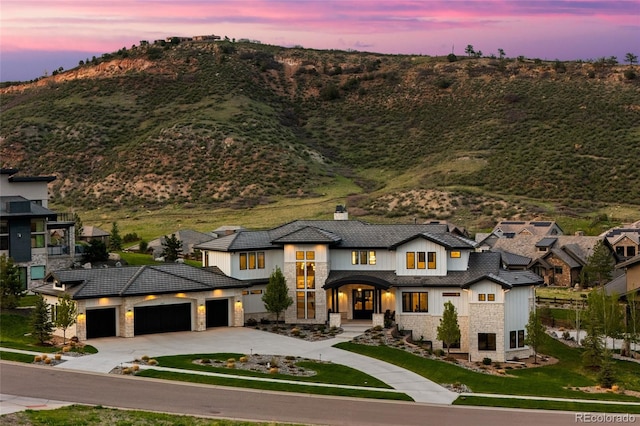 view of front of home featuring a chimney, a garage, a mountain view, concrete driveway, and stone siding