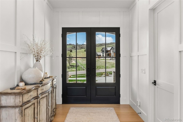 doorway with french doors, light wood finished floors, and a decorative wall