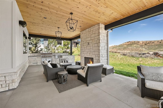 view of patio / terrace featuring grilling area, exterior kitchen, a mountain view, and an outdoor living space with a fireplace