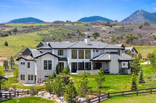 back of house featuring board and batten siding, a chimney, fence, a mountain view, and stone siding
