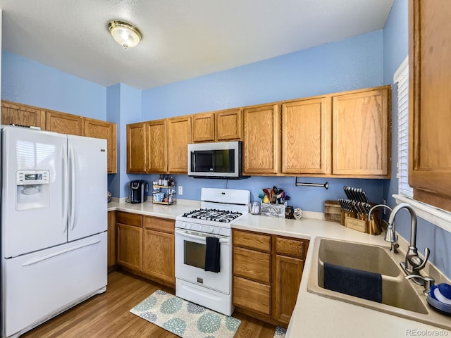 9832 Kenton Cir, Commerce City, CO 80022 - kitchen featuring white appliances, a sink, wood finished floors, and brown cabinetry