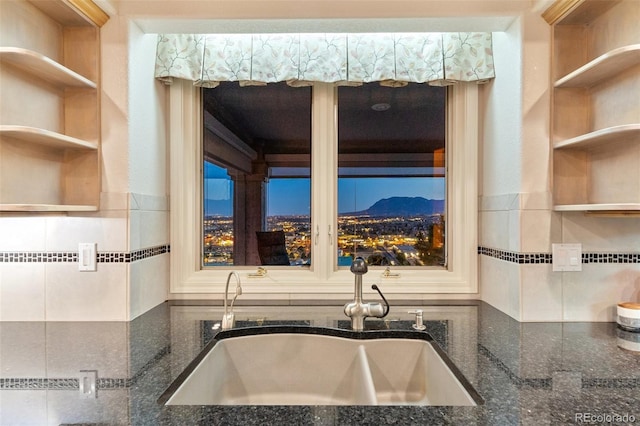 kitchen featuring open shelves, a sink, tile walls, dark stone counters, and backsplash