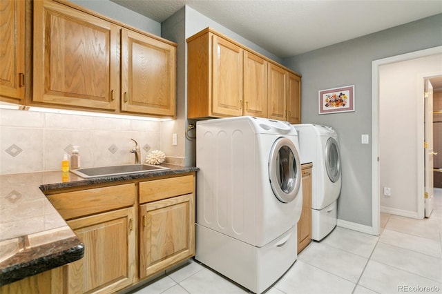washroom featuring baseboards, a sink, independent washer and dryer, cabinet space, and light tile patterned flooring