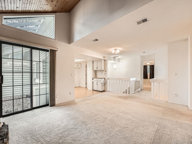 unfurnished living room with plenty of natural light, light colored carpet, wood ceiling, and a high ceiling