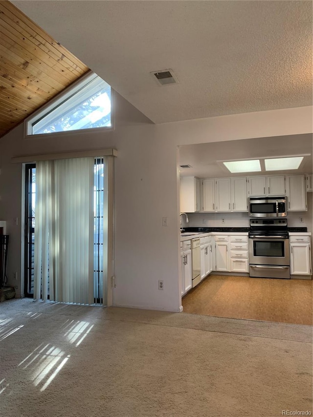 kitchen with stainless steel appliances, white cabinetry, vaulted ceiling, and light carpet