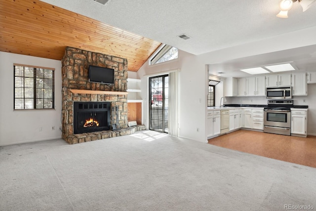 12622 E Warren Dr Unit E, Aurora, CO 80014 - kitchen featuring appliances with stainless steel finishes, open floor plan, white cabinets, a stone fireplace, and vaulted ceiling