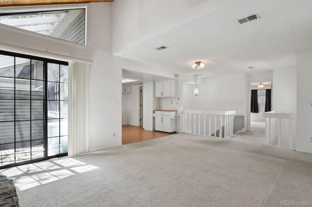 12622 E Warren Dr Unit E, Aurora, CO 80014 - unfurnished living room featuring light colored carpet, visible vents, and a towering ceiling