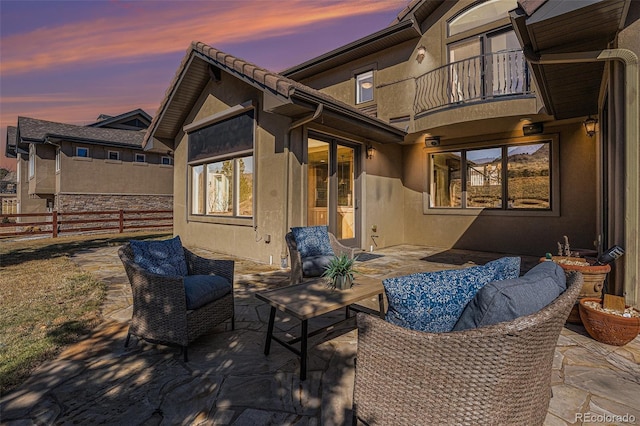 patio terrace at dusk featuring fence and a balcony