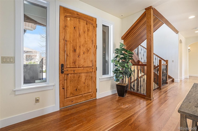 entrance foyer featuring baseboards, stairs, arched walkways, and wood finished floors